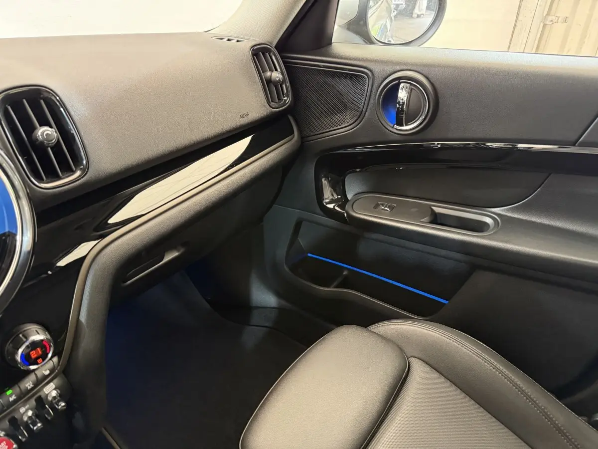 Vue intérieure côté passager de la MINI Countryman gris clair 2023, tableau de bord et porte avec éclairage d'ambiance bleu.