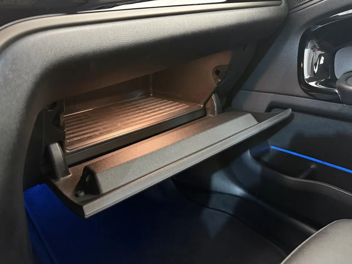 Gros plan sur la boîte à gants ouverte côté passager du MINI Countryman 2023 avec éclairage d'ambiance bleu.