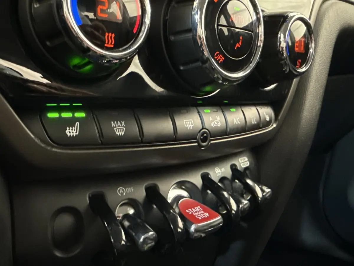 Gros plan sur la console centrale du MINI Countryman gris clair 2023, avec boutons de climatisation et bouton start/stop rouge.