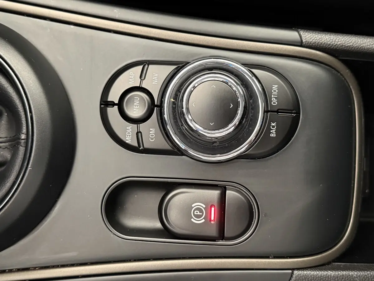 Vue rapprochée de la molette de commande multimédia et du frein à main électrique sur la console centrale d’une MINI Countryman gris clair.