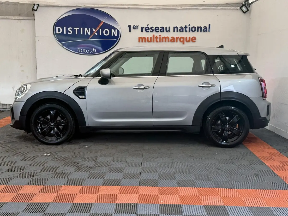 Vue de profil côté gauche d'une MINI Countryman Cooper Essential gris clair avec jantes noires dans un showroom.