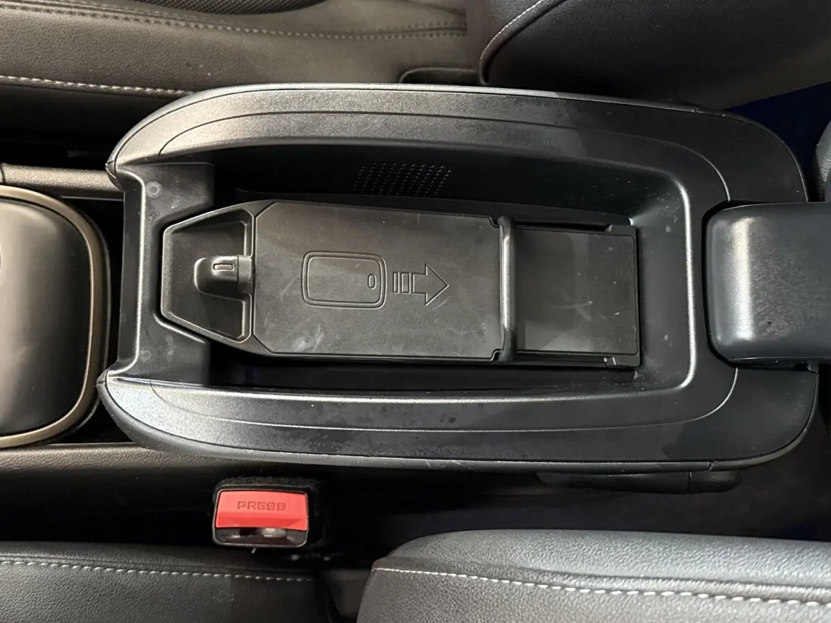 Vue rapprochée du rangement central noir avec porte coulissante et bouton de ceinture rouge dans le MINI Countryman gris clair.