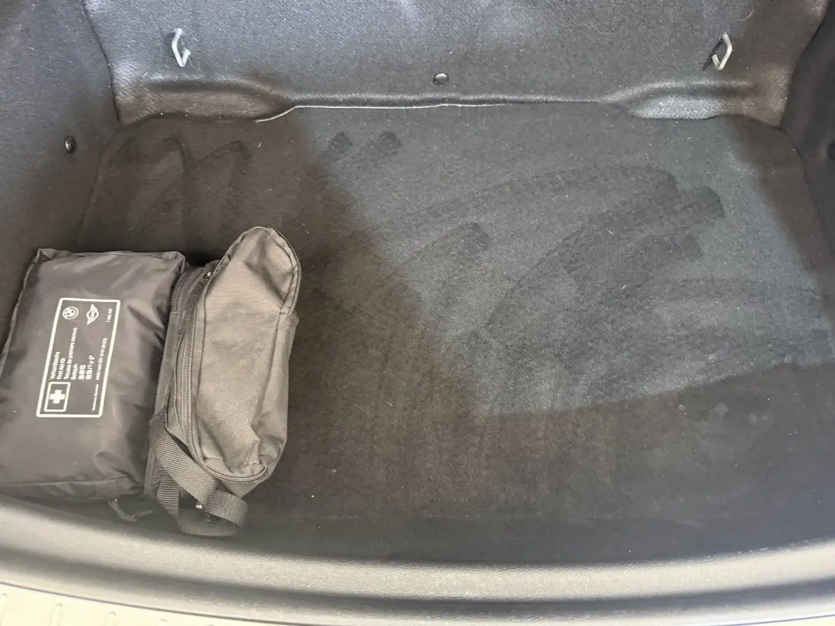 Coffre ouvert d’une MINI Countryman gris clair, vue plongeante montrant un tapis noir et deux trousses noires rangées à gauche.