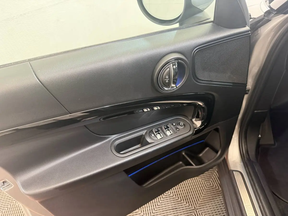 Détail de la porte avant gauche d’une MINI Countryman gris clair, montrant les commandes des vitres et le haut-parleur.