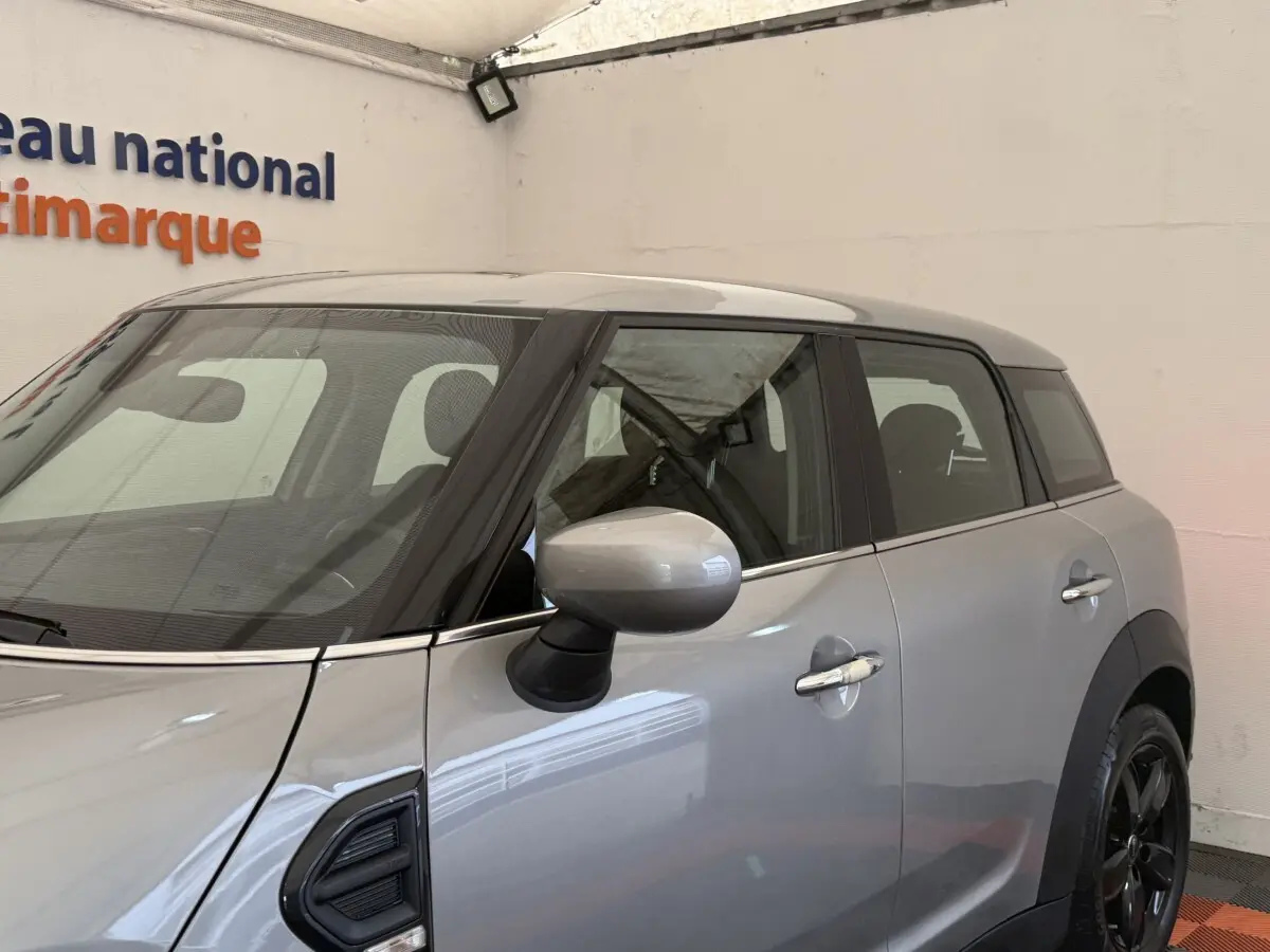 Vue de côté droit d'une MINI Countryman Cooper Essential gris clair avec rétroviseur assorti et jantes noires.