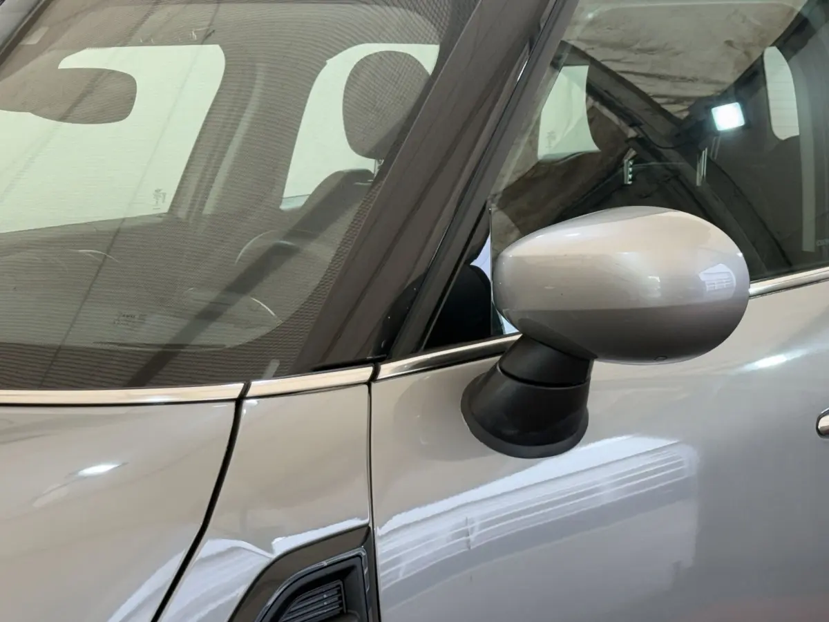 Gros plan sur le rétroviseur côté conducteur d'une MINI Countryman gris clair 2023, avec reflet sur la portière.
