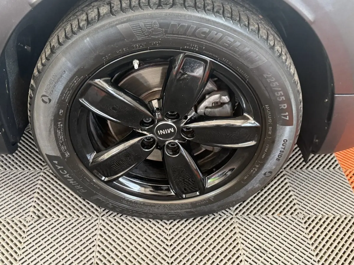 Gros plan sur la roue avant droite du MINI Countryman gris clair, jante noire brillante à cinq branches.