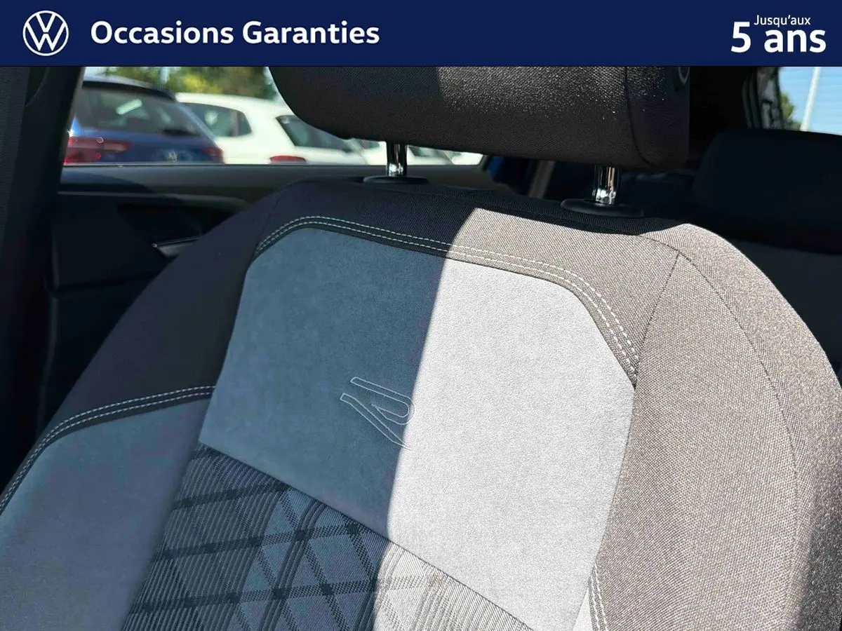 Détail du siège avant en tissu gris avec surpiqûres blanches et logo R embossé, intérieur Volkswagen Taigo 2025.