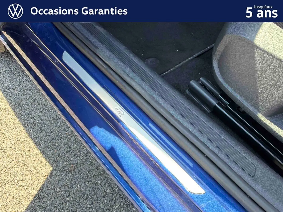 Gros plan sur la porte côté gauche d’un Volkswagen Taigo bleu métallisé avec seuil de porte en métal.