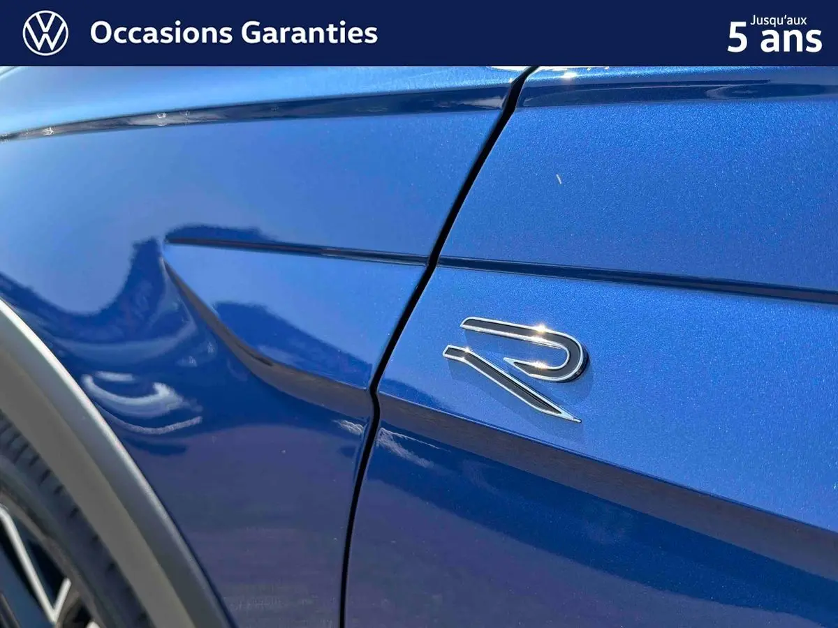 Gros plan sur l'aile avant droite bleue métallisée d'un Volkswagen Taigo avec logo R brillant.
