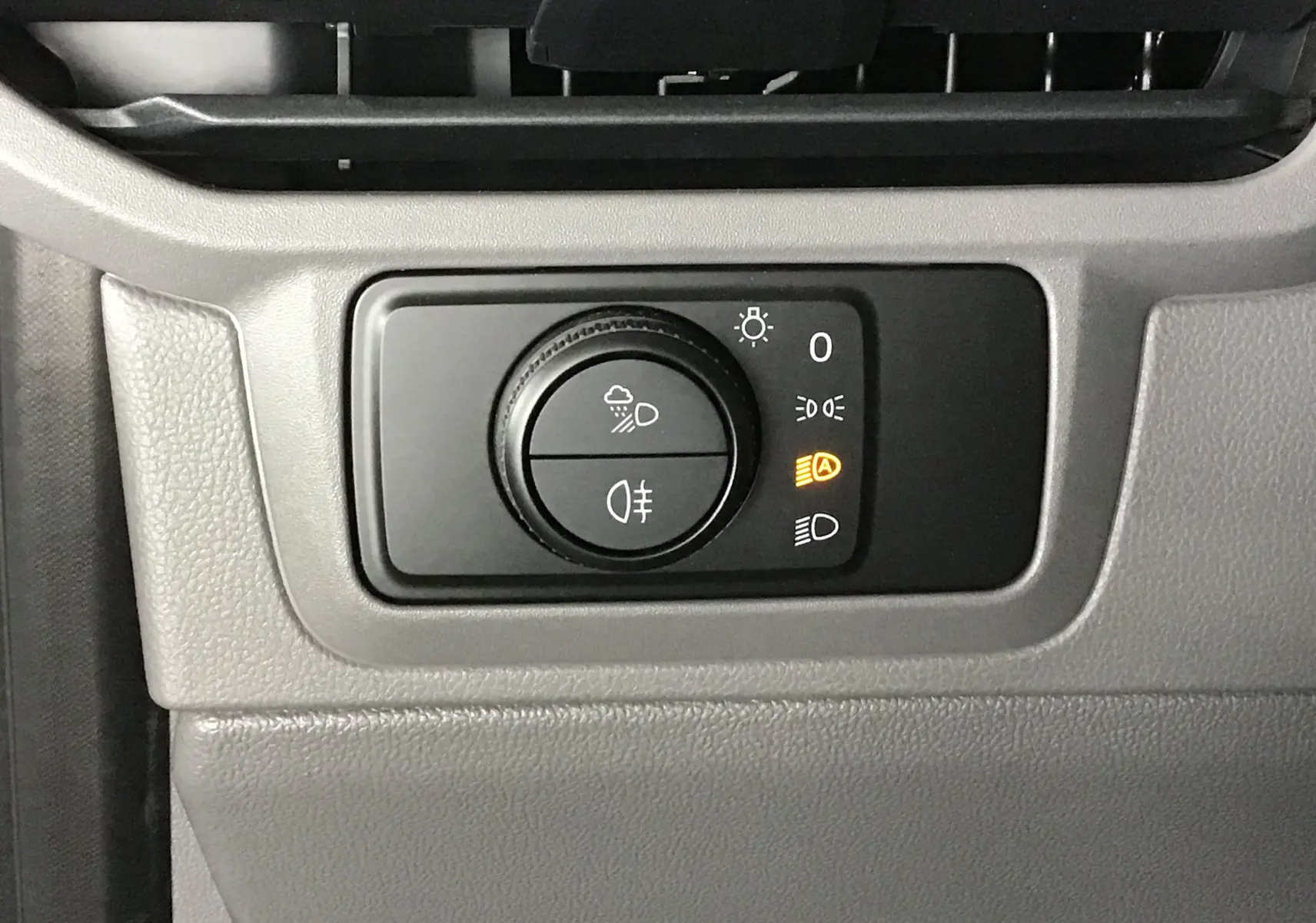 Gros plan sur le bouton de commande des phares du Volkswagen Transporter T7 gris anthracite, tableau de bord intérieur.