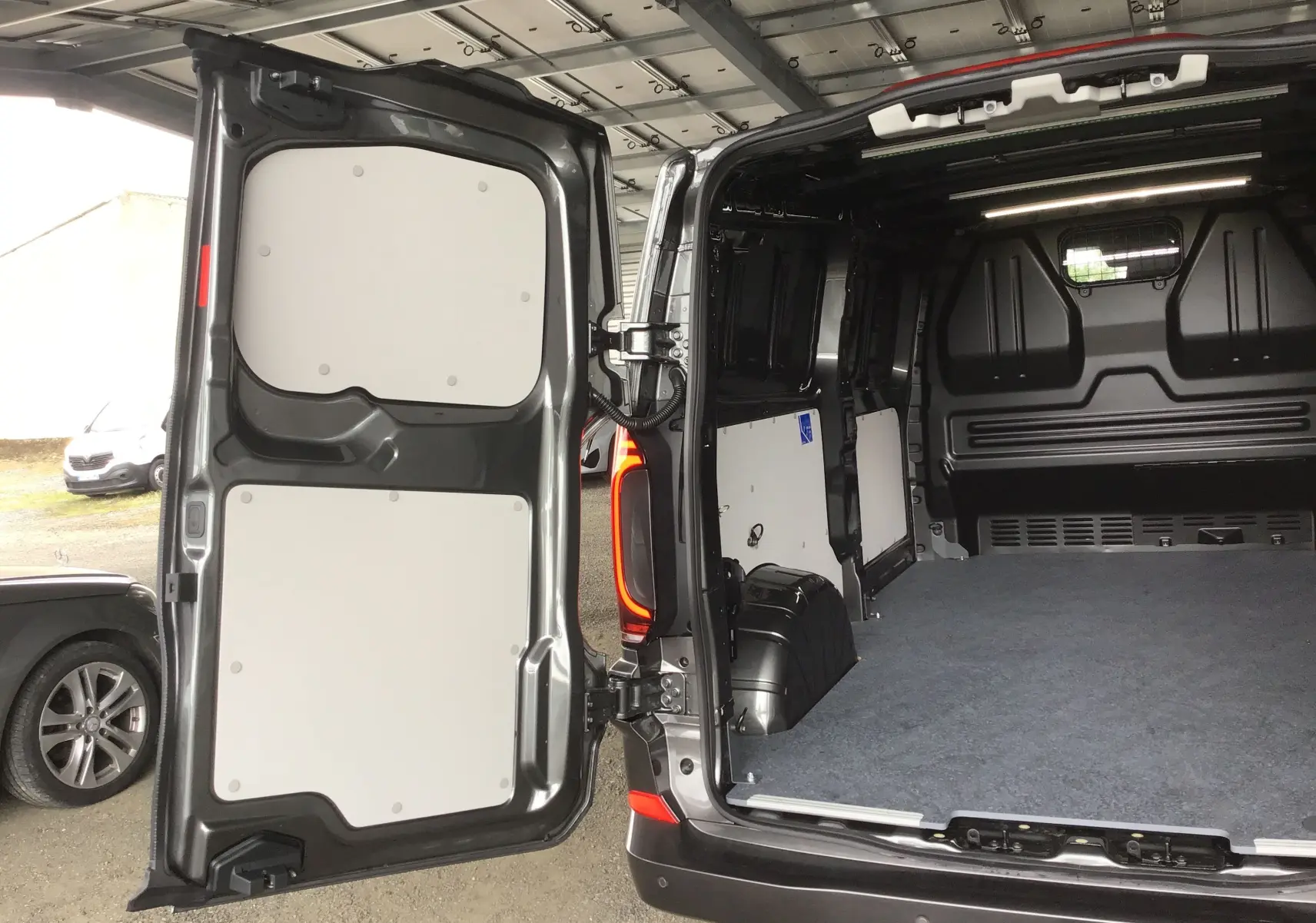 Vue arrière ouverte du Volkswagen Transporter T7 gris anthracite montrant l'espace de chargement vide et les portes battantes.