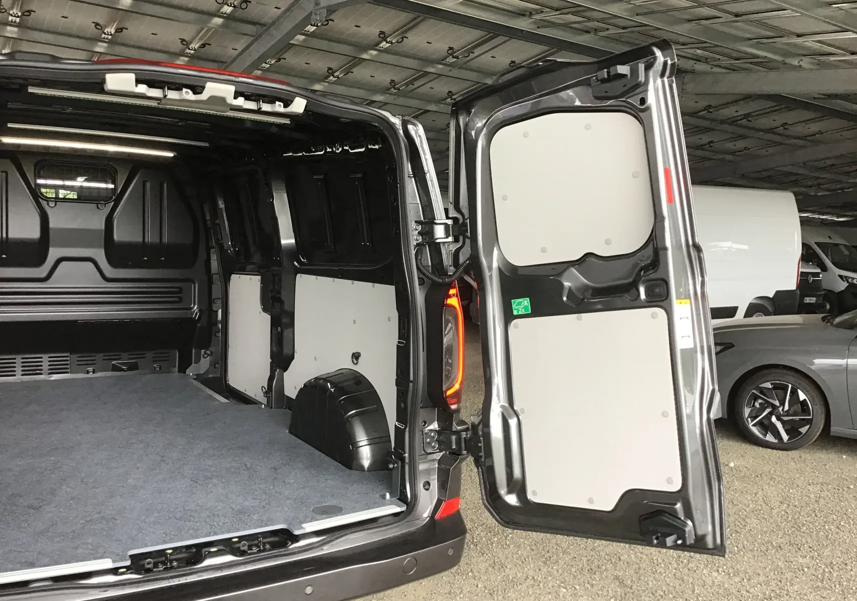 Vue arrière ouverte du Volkswagen Transporter T7 gris anthracite montrant l'espace de chargement intérieur et les portes battantes.