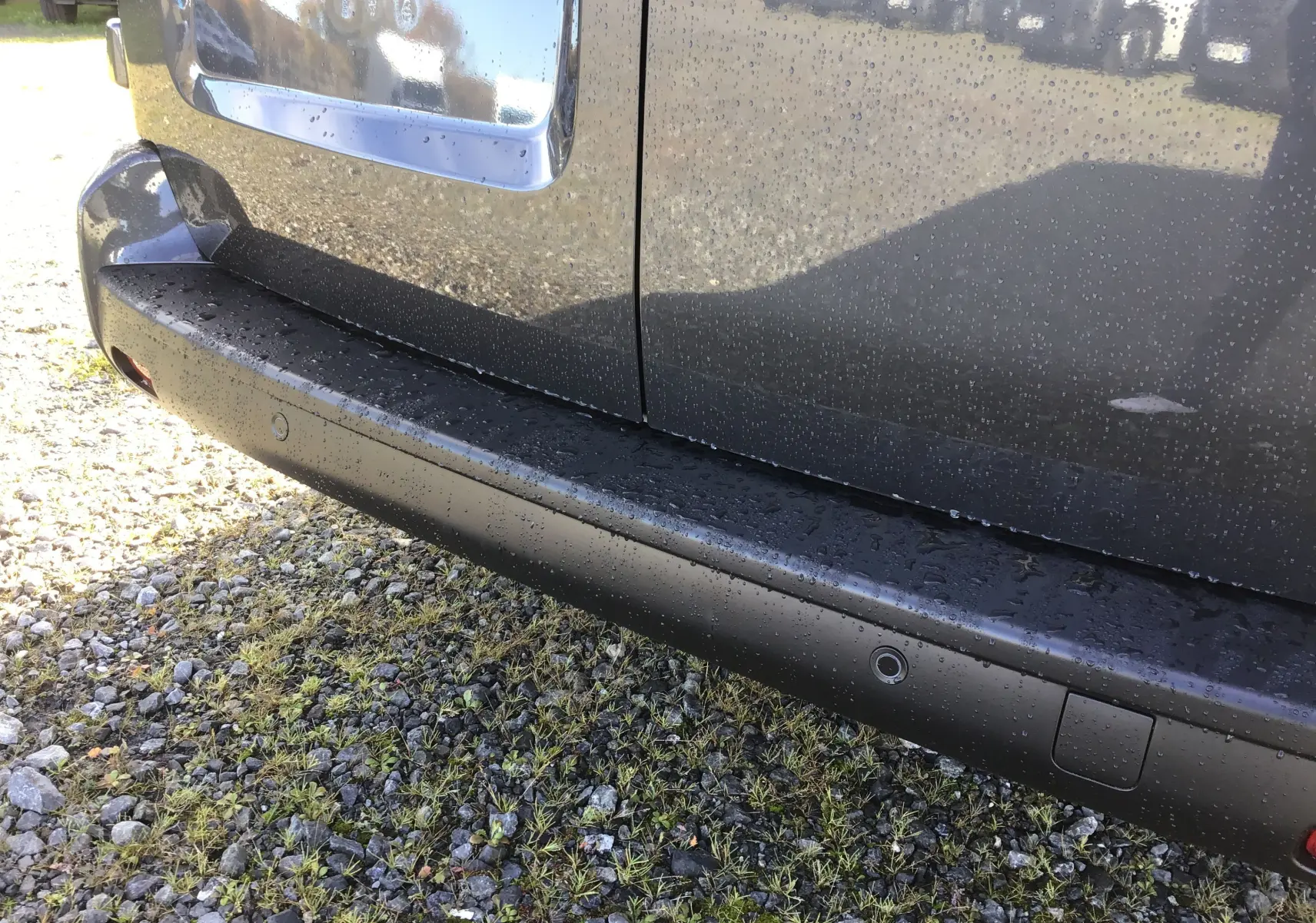 Gros plan sur la partie basse côté droit d'un Citroën Jumpy gris titane avec capteurs de stationnement et gouttes d'eau.