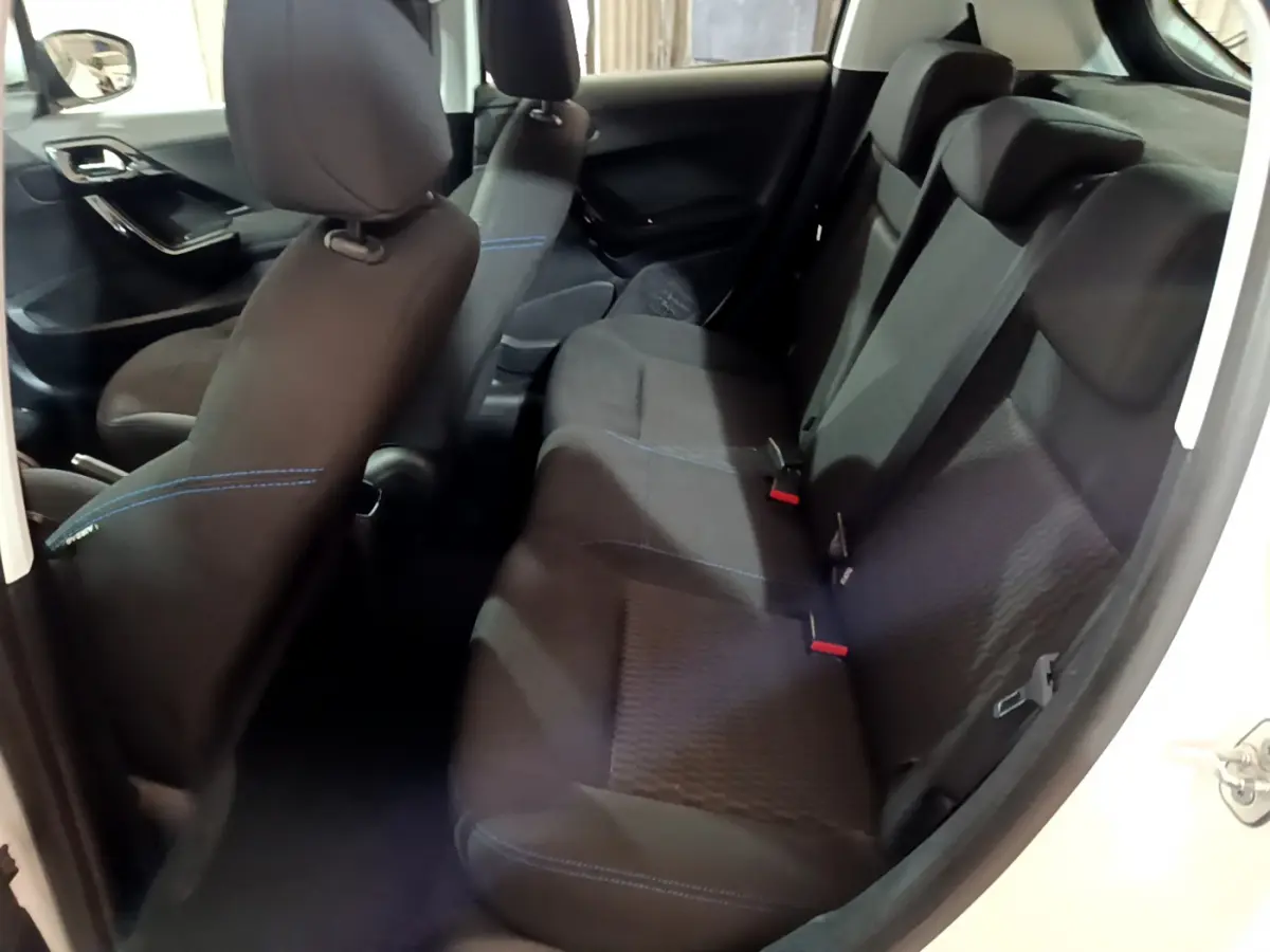 Vue intérieure côté droit montrant la banquette arrière noire avec surpiqûres bleues d'une Peugeot 208 blanche Puretech 82 Signature 2018.
