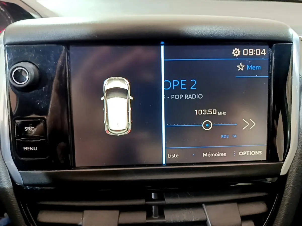 Écran tactile central de la Peugeot 208 Puretech 82 Signature affichant la radio et la vue du véhicule blanc en survol.