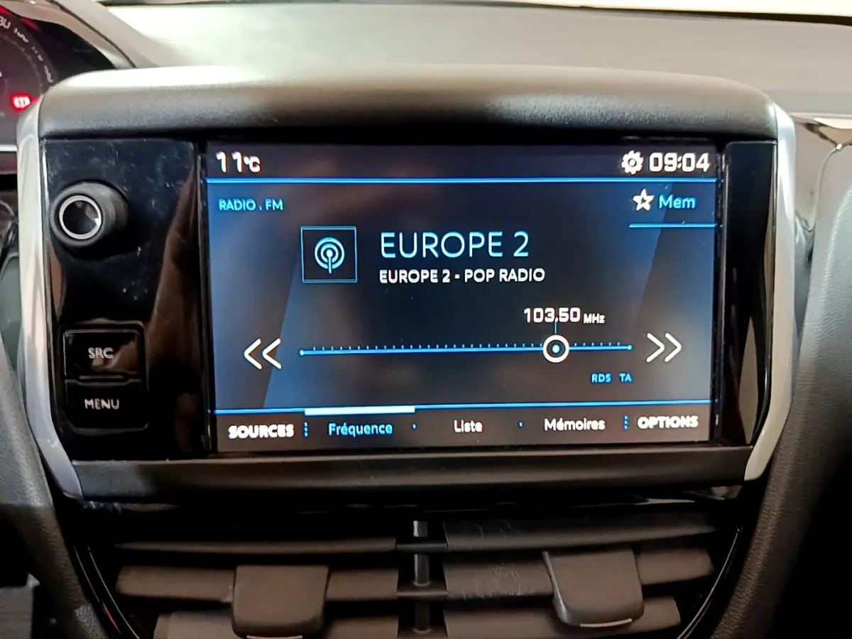 Écran tactile central du tableau de bord du Peugeot 208 blanc, affichant la radio Europe 2 à 103,5 MHz.