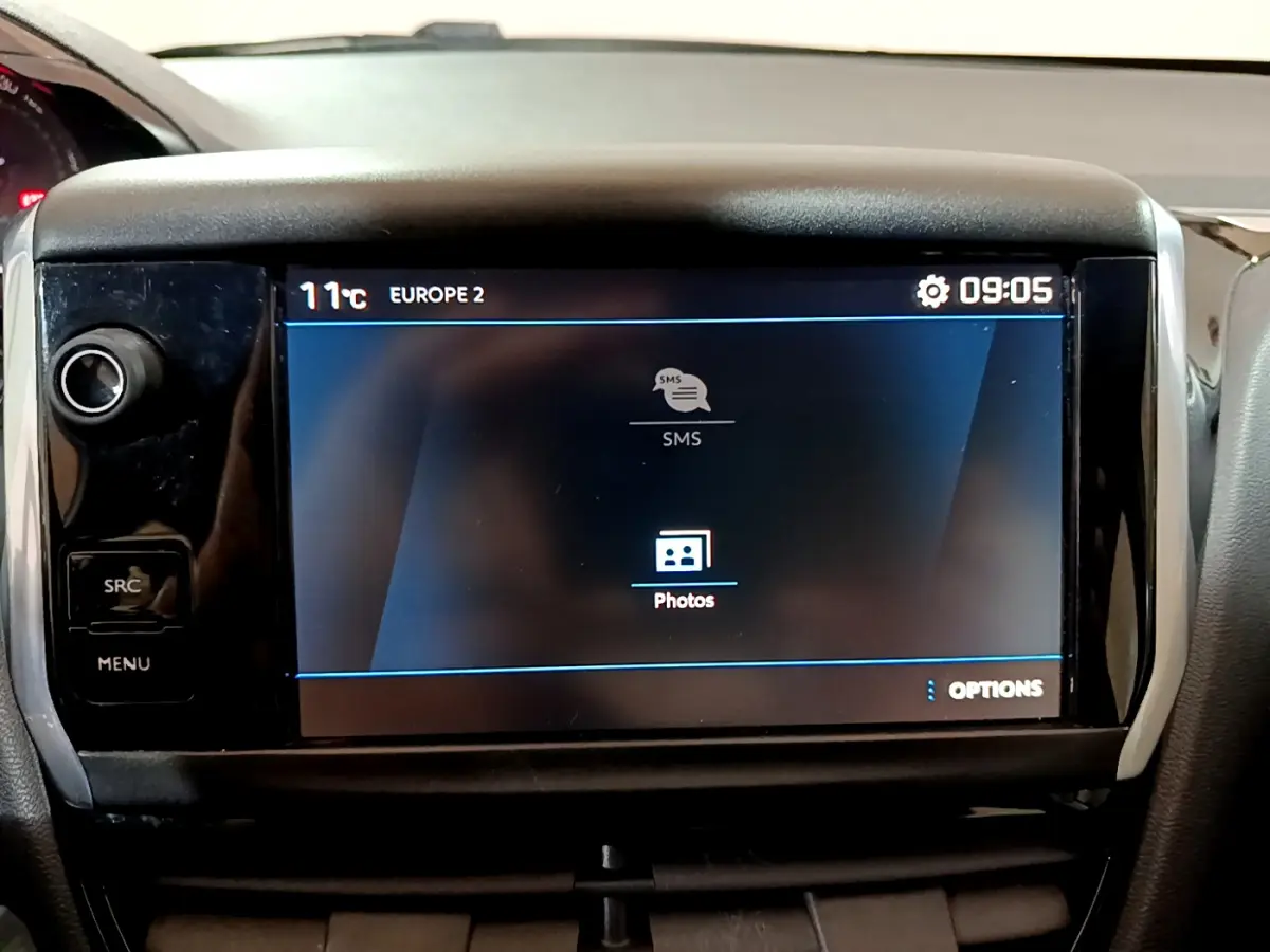 Écran tactile central allumé du tableau de bord d'une Peugeot 208 Puretech 82 Signature, intérieur noir.