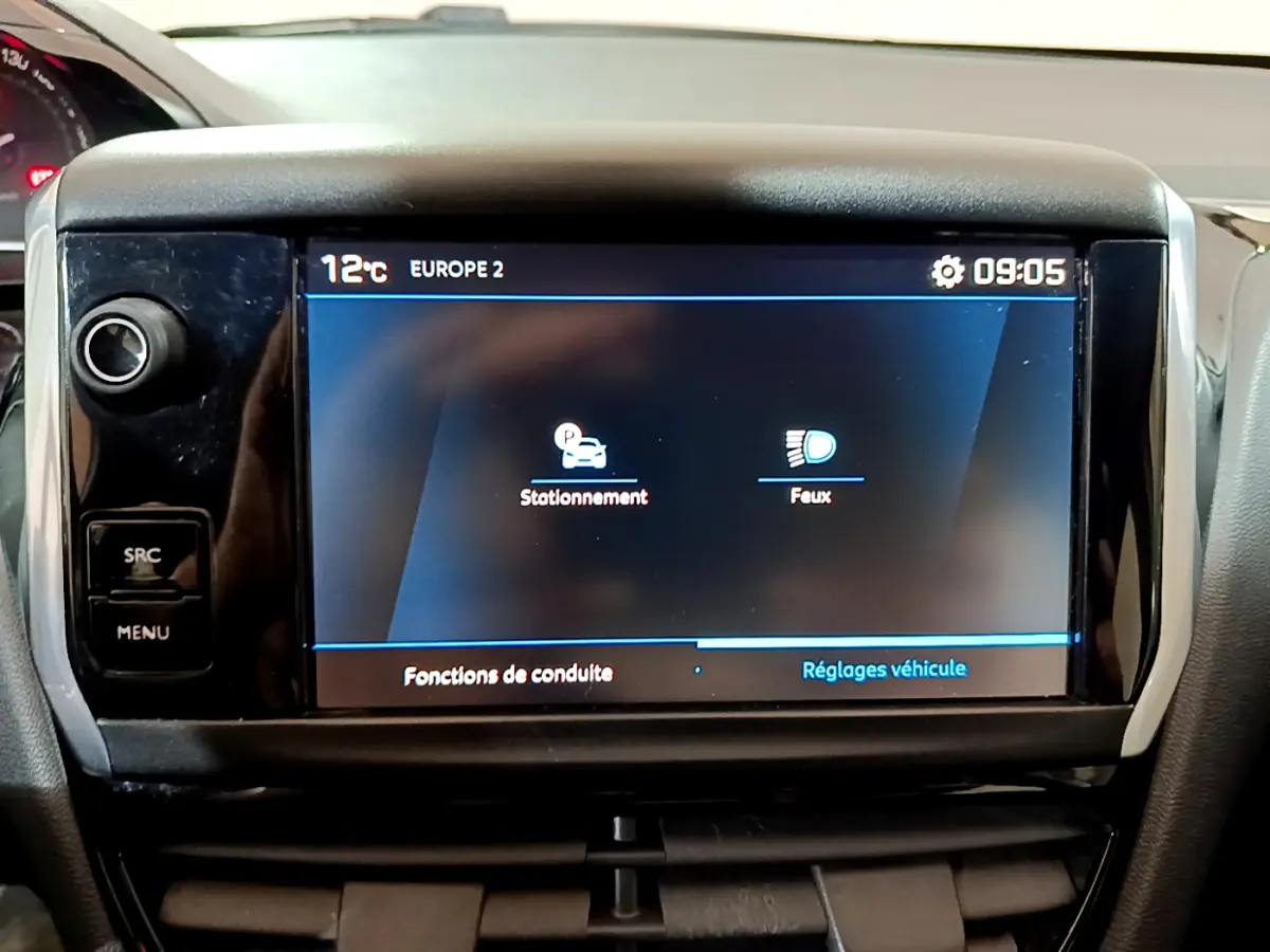 Écran tactile central du tableau de bord de la Peugeot 208 blanche, affichant les réglages de stationnement et feux.