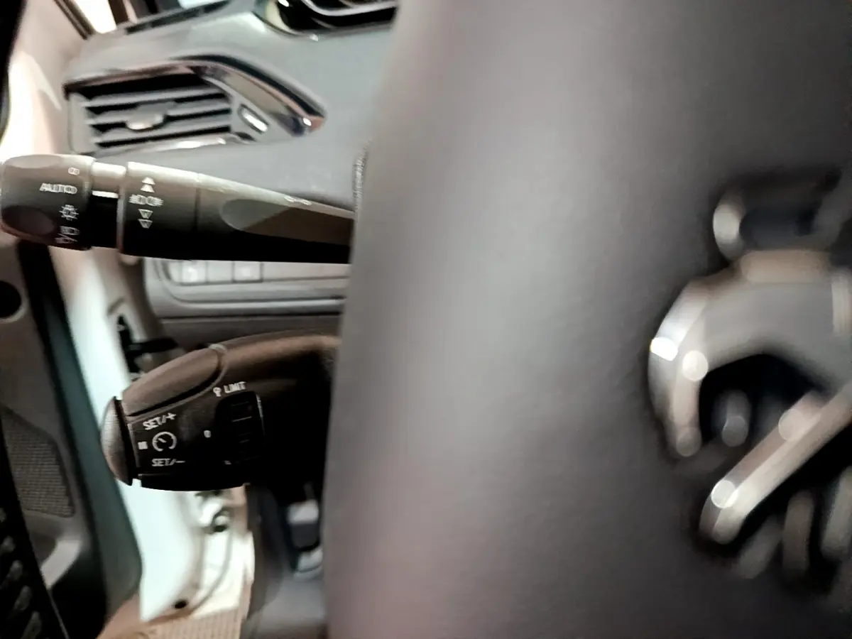 Gros plan sur le volant cuir noir et les commandes de régulateur de vitesse d'une Peugeot 208 blanche Puretech 82 Signature.