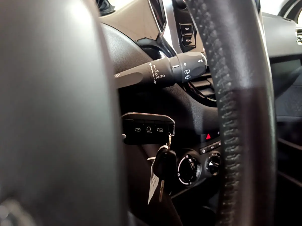 Gros plan sur le volant cuir et la clé insérée dans le contacteur d'une Peugeot 208 Puretech 82 Signature, intérieur noir.