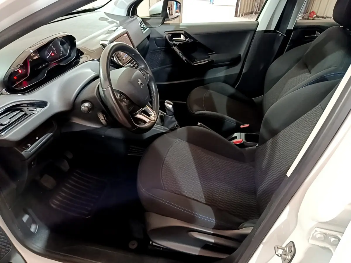 Intérieur avant droit de la Peugeot 208 blanche, volant cuir, tableau de bord numérique et sièges tissu noirs.