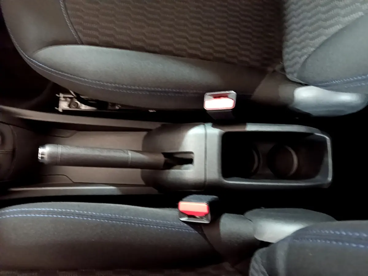 Vue plongeante sur la console centrale noire avec frein à main et porte-gobelets entre les sièges tissu bleu de la Peugeot 208 blanche