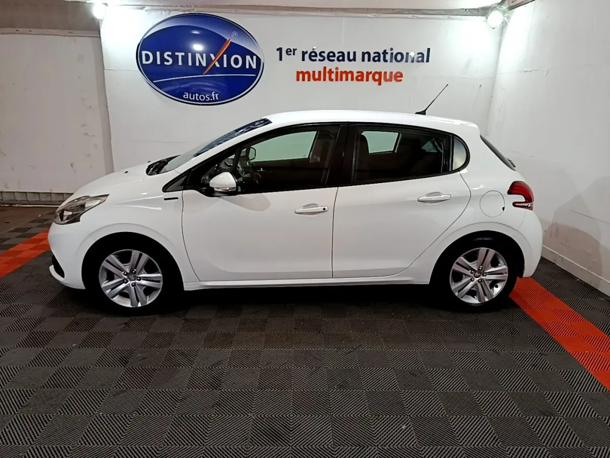 Peugeot 208 Puretech 82 Signature blanc vue de profil côté gauche dans un showroom avec logo Distinxion en arrière-plan.