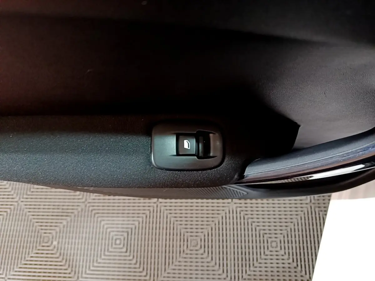 Gros plan sur le bouton de commande de la vitre électrique côté porte intérieure d'une Peugeot 208 blanche de 2018.