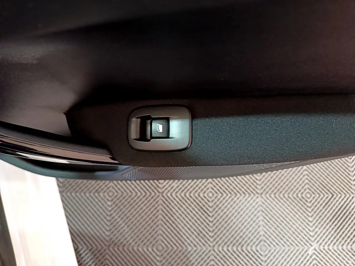 Gros plan sur le bouton de commande de la vitre électrique dans la portière intérieure noire d'une Peugeot 208 blanche.
