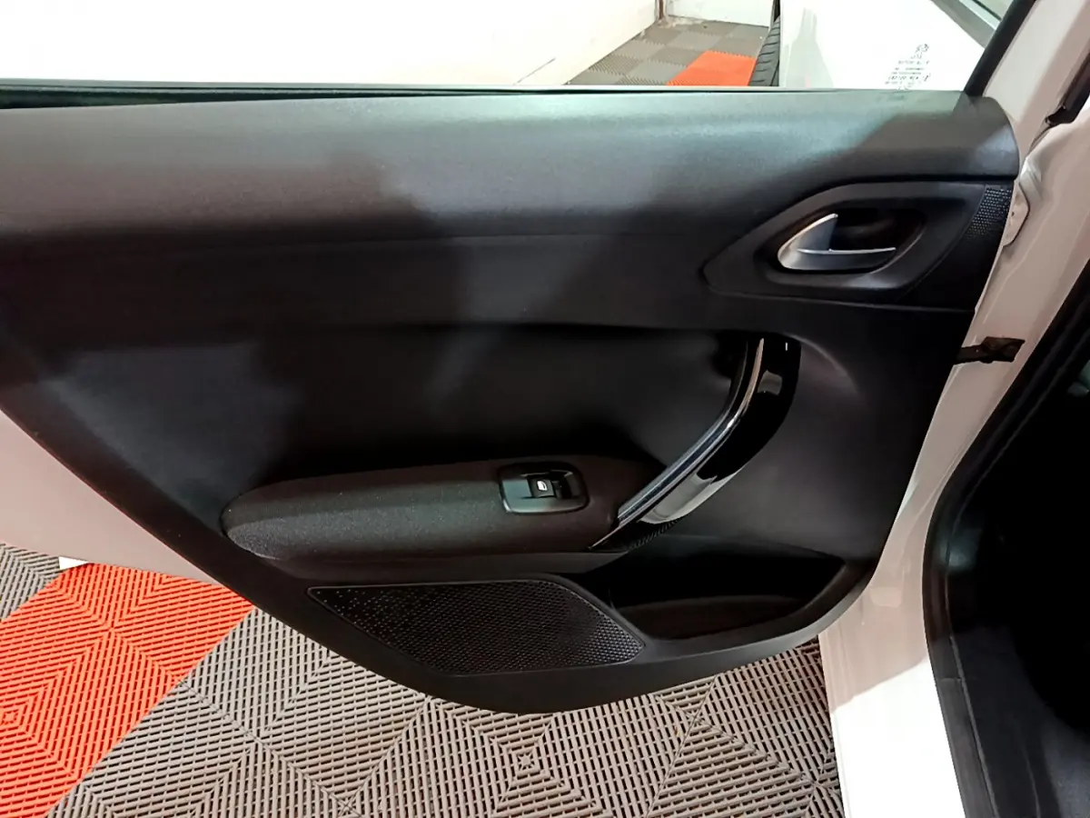 Vue intérieure de la porte côté droit d'une Peugeot 208 blanche avec poignée chromée et commande de vitre électrique.