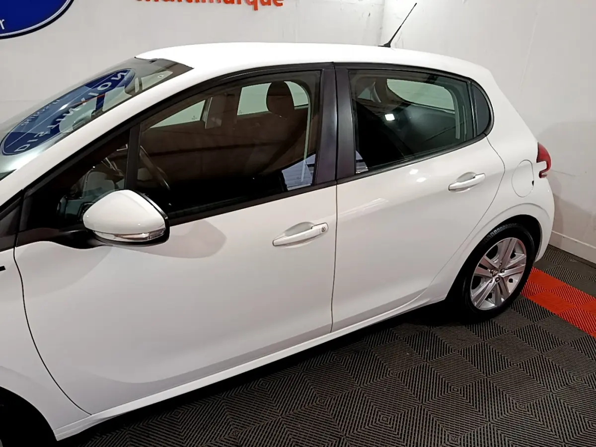 Profil côté gauche d'une Peugeot 208 Puretech 82 Signature blanche, avec rétroviseurs chromés et jantes alliage visibles.