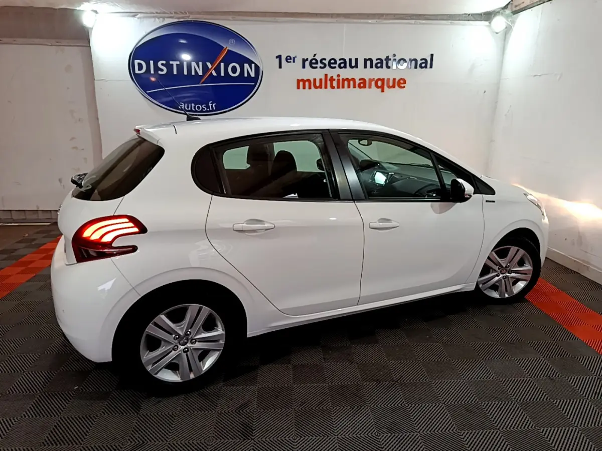 Peugeot 208 Puretech 82 Signature blanc vue de profil côté gauche avec feux arrière allumés en intérieur showroom.