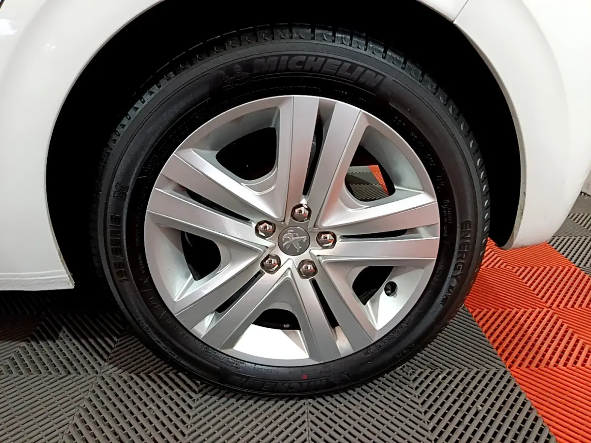 Gros plan sur la roue avant droite d'une Peugeot 208 blanche, mettant en valeur la jante alliage et le pneu Michelin.