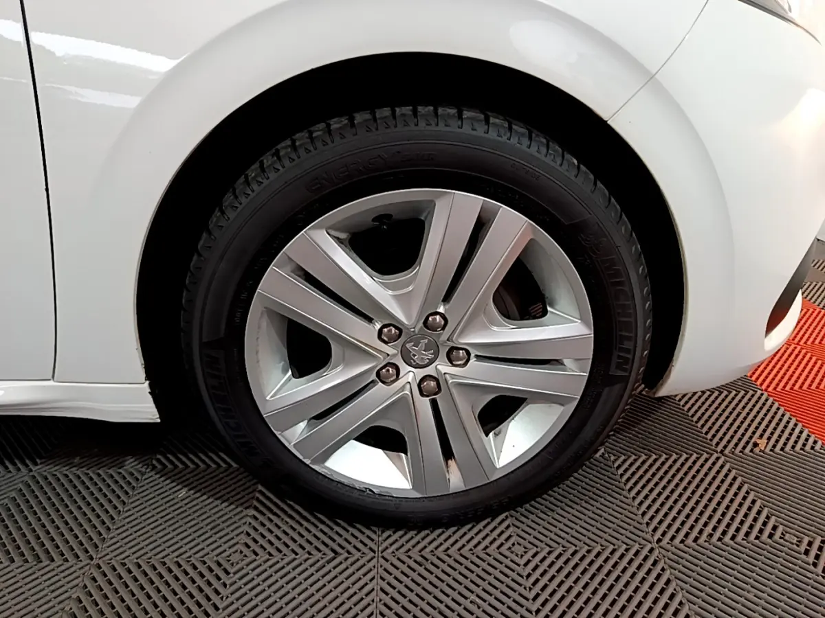 Gros plan sur la roue avant gauche d'une Peugeot 208 blanche, mettant en valeur la jante alliage et le pneu Michelin.