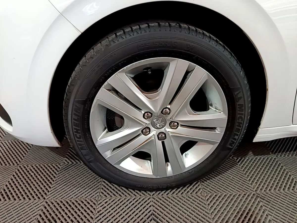 Gros plan sur la roue avant droite d'une Peugeot 208 blanche, mettant en valeur la jante alliage et le pneu Michelin.