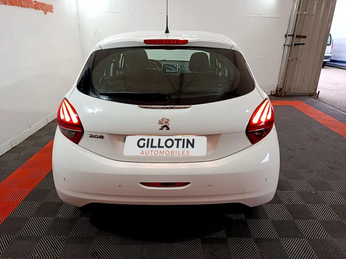 Vue arrière d'une Peugeot 208 blanche avec feux arrière allumés dans un garage intérieur.