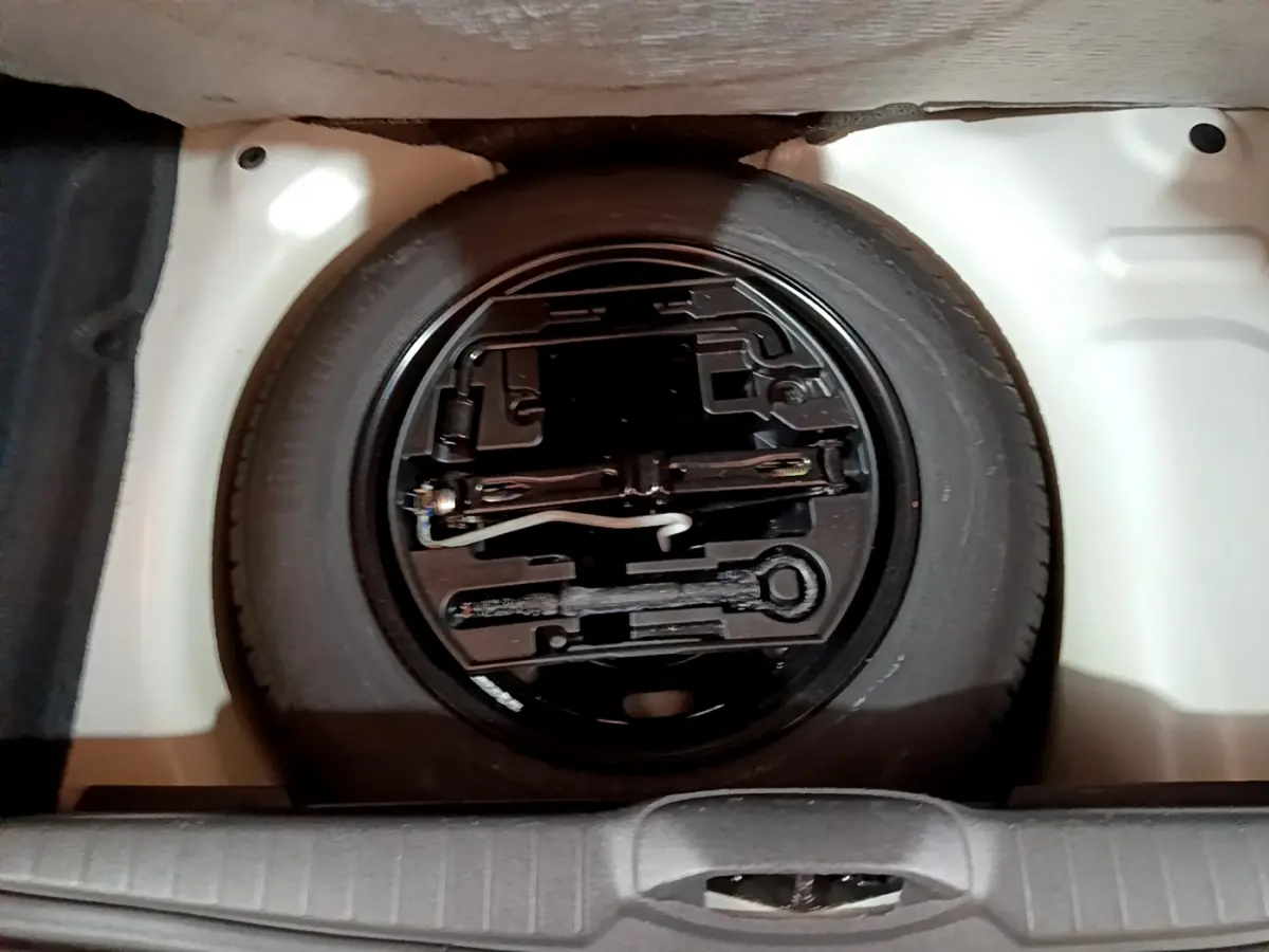 Roue de secours noire avec outils de bord dans le coffre blanc d'une Peugeot 208 Puretech 82 Signature 2018.