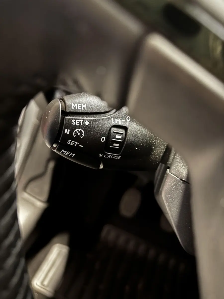 Gros plan sur la commande de régulateur de vitesse noire dans l'habitacle d'une Peugeot 208 gris clair 2024 PureTech Active.