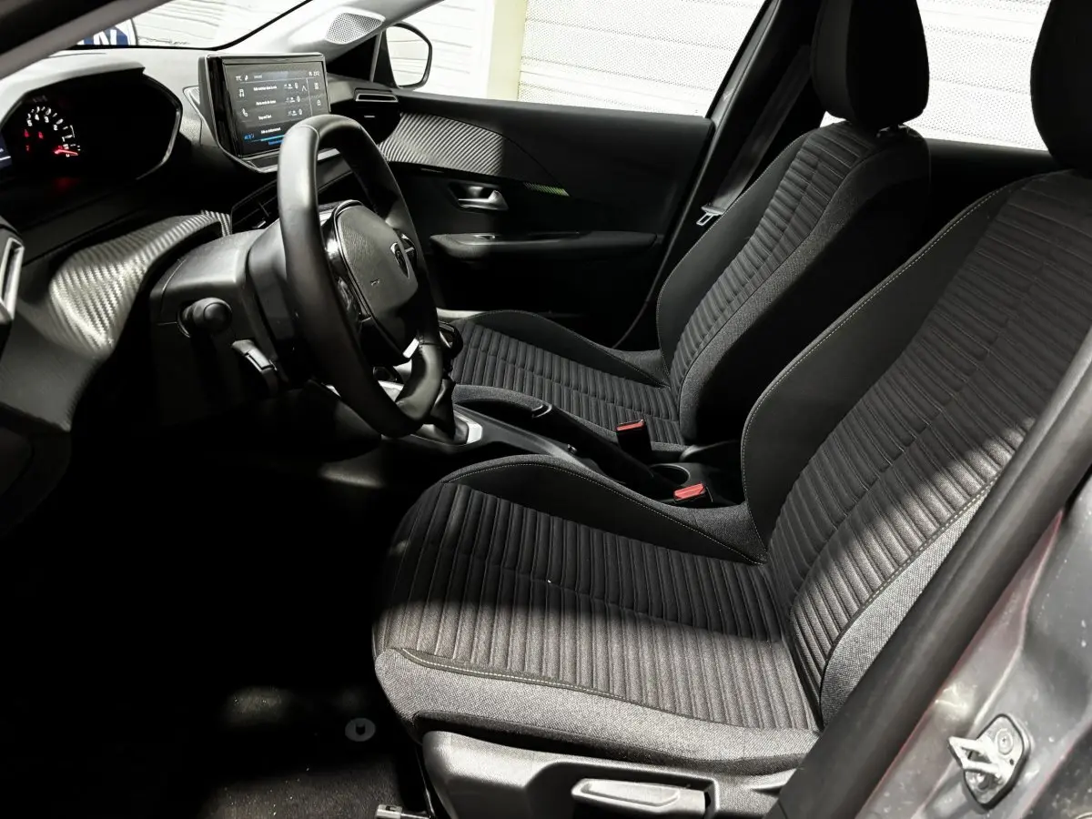 Intérieur avant droit de la Peugeot 208 gris clair 2024, sièges tissu noirs et tableau de bord avec écran tactile.