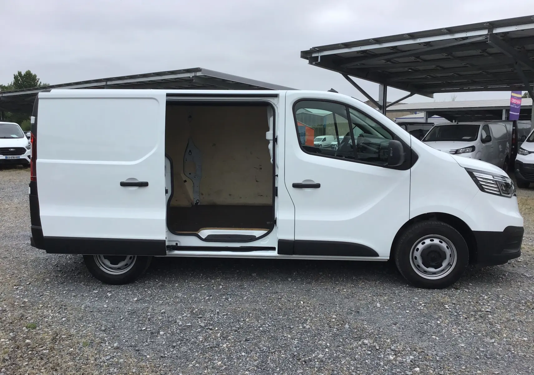 Vue de profil côté gauche d’un Renault Trafic Fourgon blanc 2024 avec porte latérale coulissante ouverte montrant l’intérieur vide.