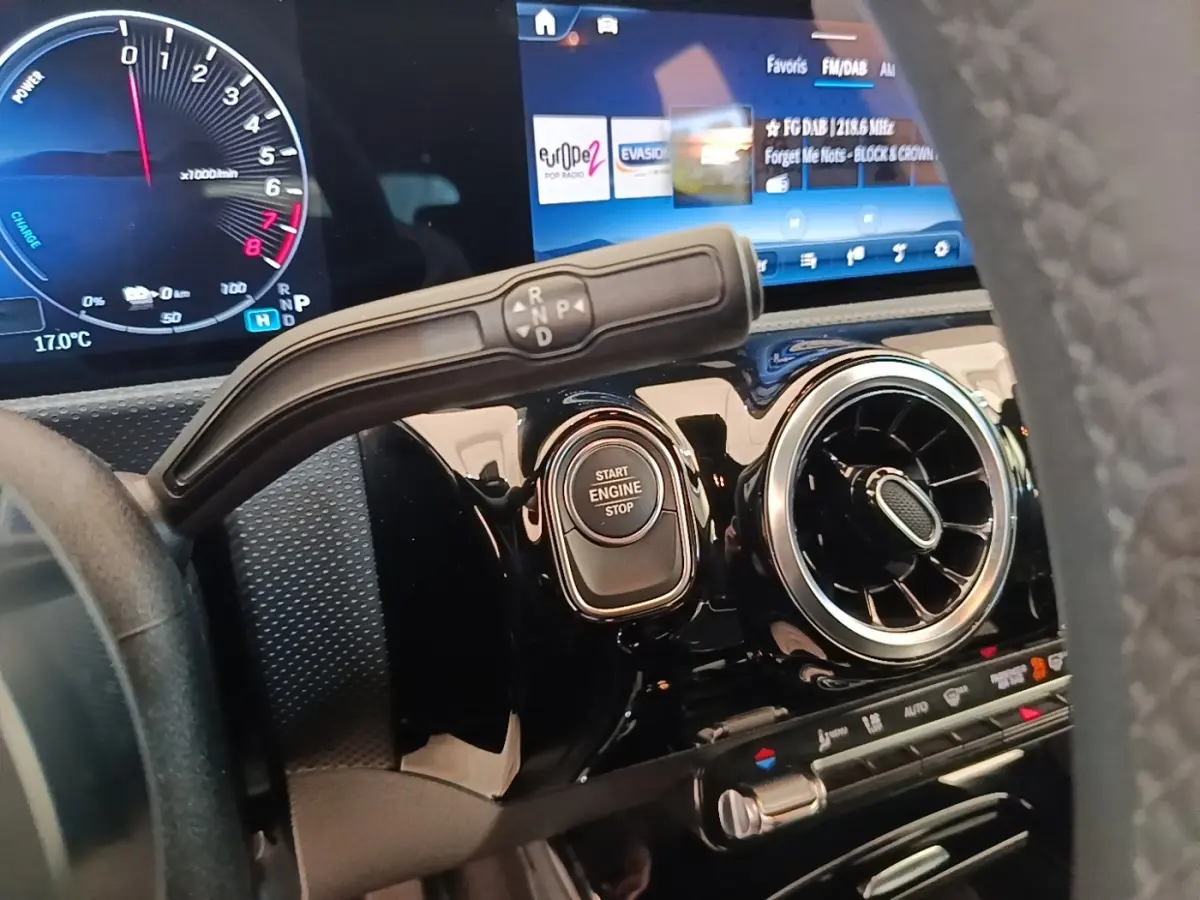 Gros plan intérieur sur le tableau de bord noir brillant de la Mercedes Classe A 250 e, avec bouton start/stop et écran tactile.