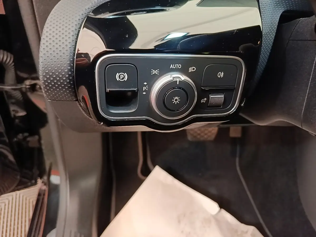 Gros plan sur les commandes d’éclairage et frein à main électrique dans une Mercedes Classe A noire, côté gauche.