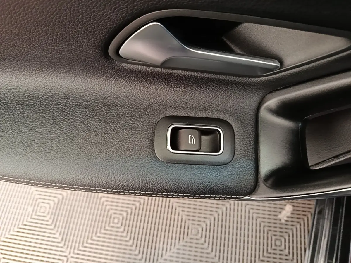 Gros plan sur la commande de la vitre électrique côté conducteur, garniture noire avec surpiqûres blanches.