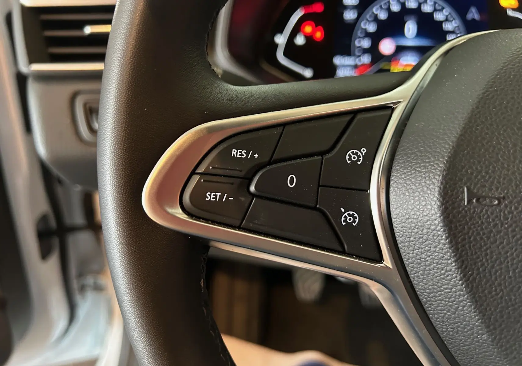 Gros plan sur les commandes de régulateur de vitesse au volant noir d'une Renault Clio V 2021.