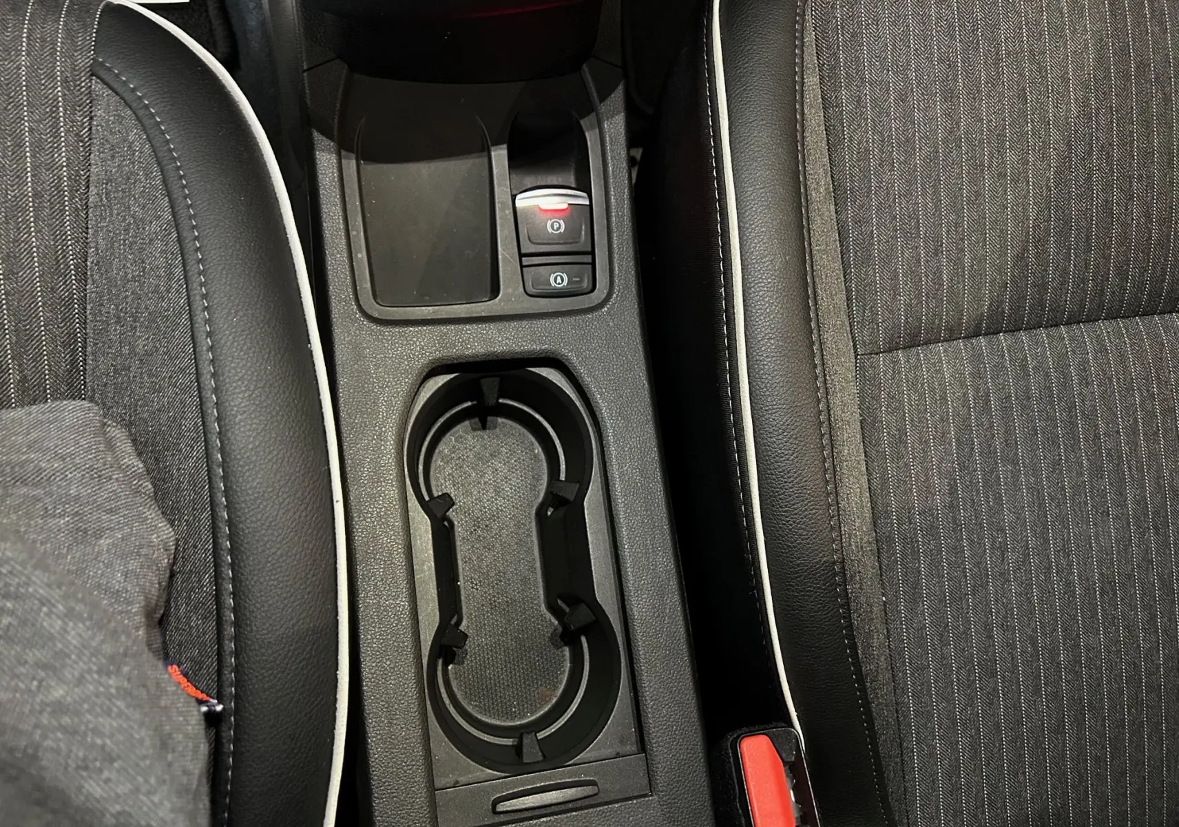 Gros plan sur la console centrale avec porte-gobelets et sièges en tissu noir à surpiqûres blanches de la Renault Clio V.