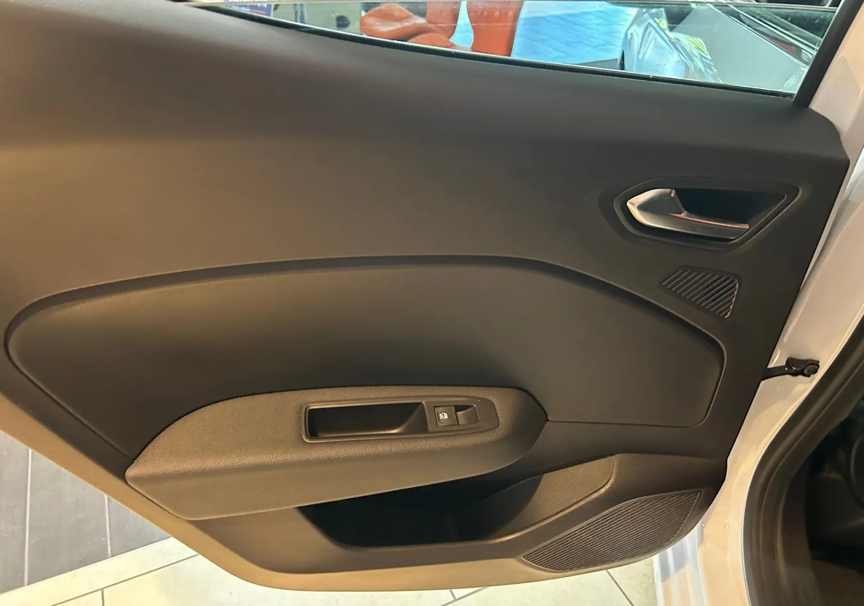 Vue intérieure sur la porte côté droit d'une Renault Clio V blanche nacrée, avec poignée et commande de vitre noire.