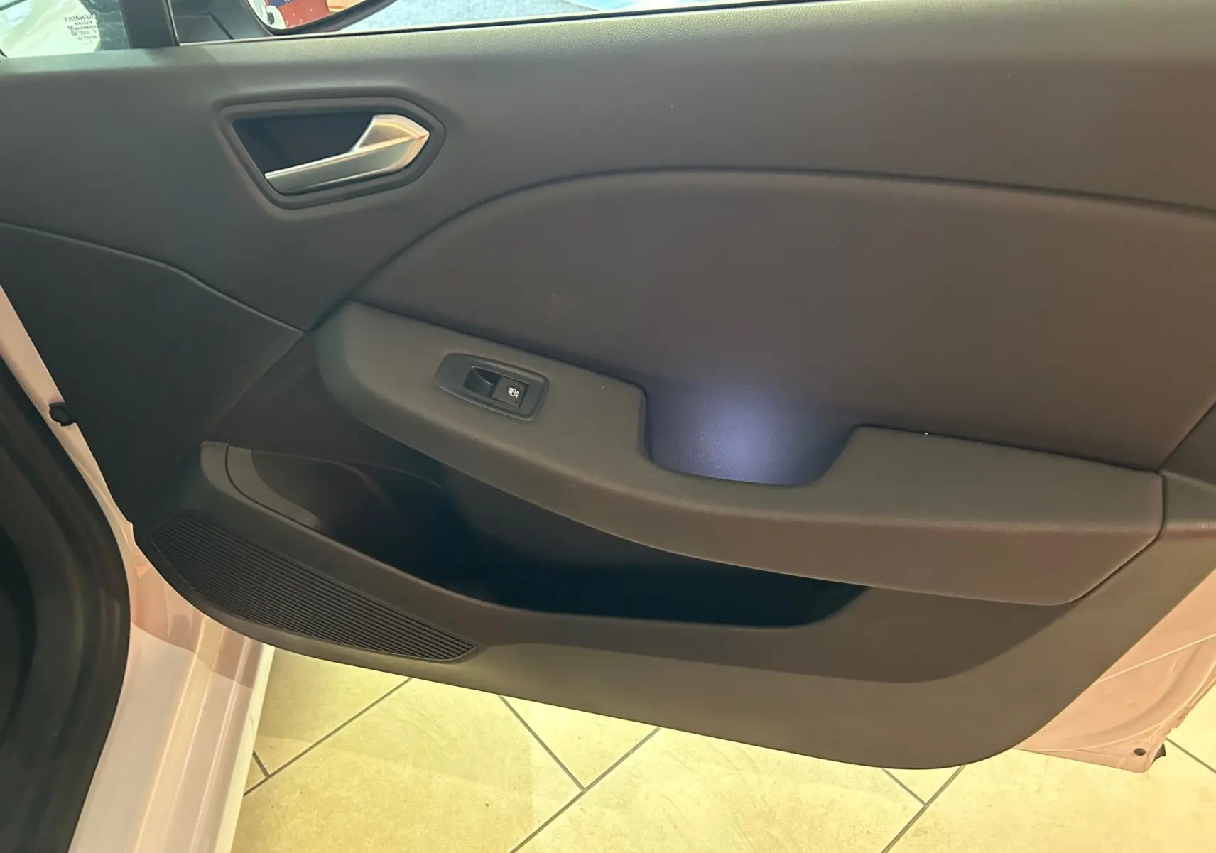 Vue rapprochée de la porte avant gauche de la Renault Clio V blanc nacré, avec poignée et commande de vitre électrique.