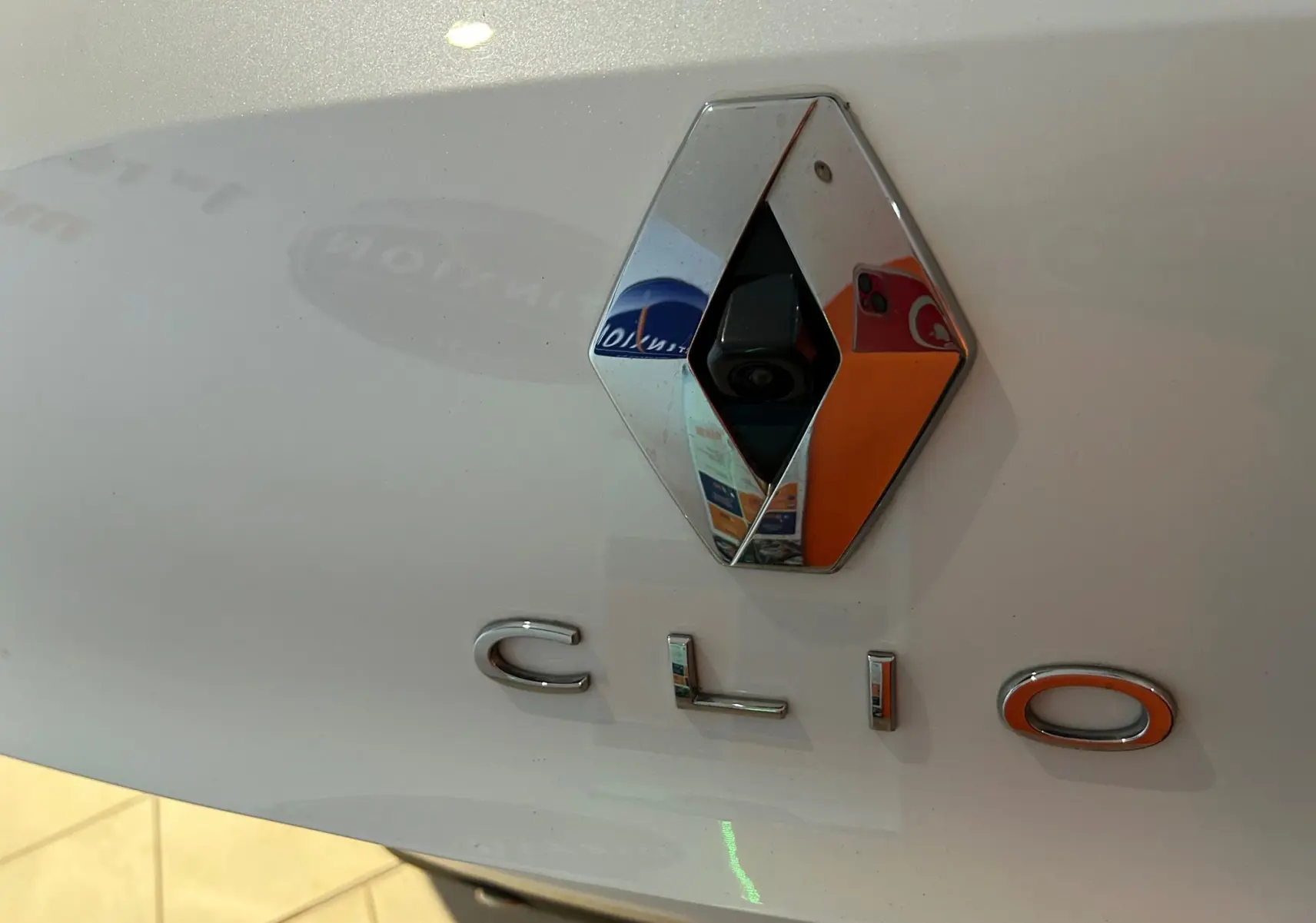 Gros plan sur le logo Renault et l’inscription Clio sur la malle arrière d’une Clio V blanc nacré métallisé.