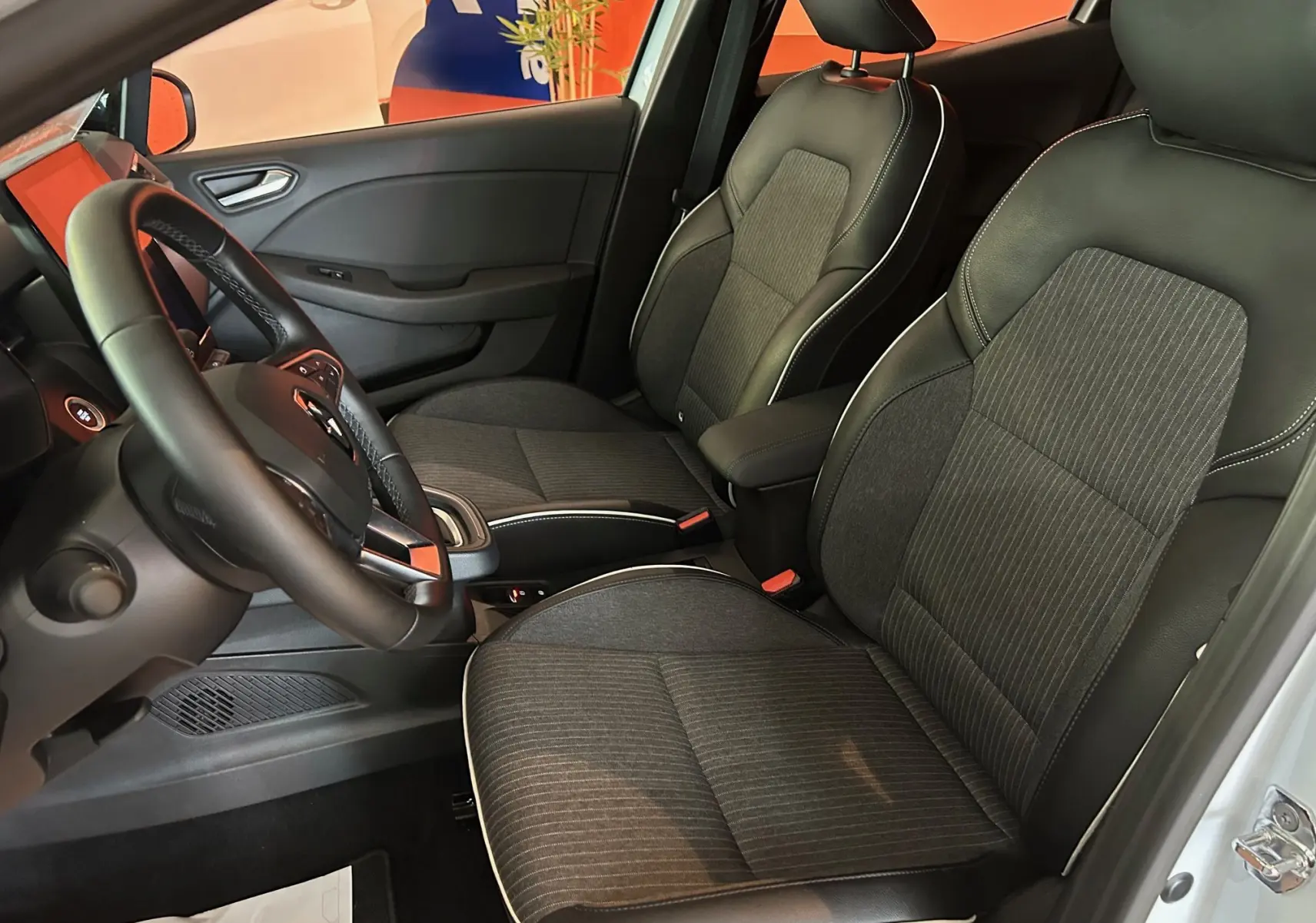 Intérieur de la Renault Clio V blanc nacré, vue côté conducteur montrant sièges tissu et cuir noir avec surpiqûres blanches.